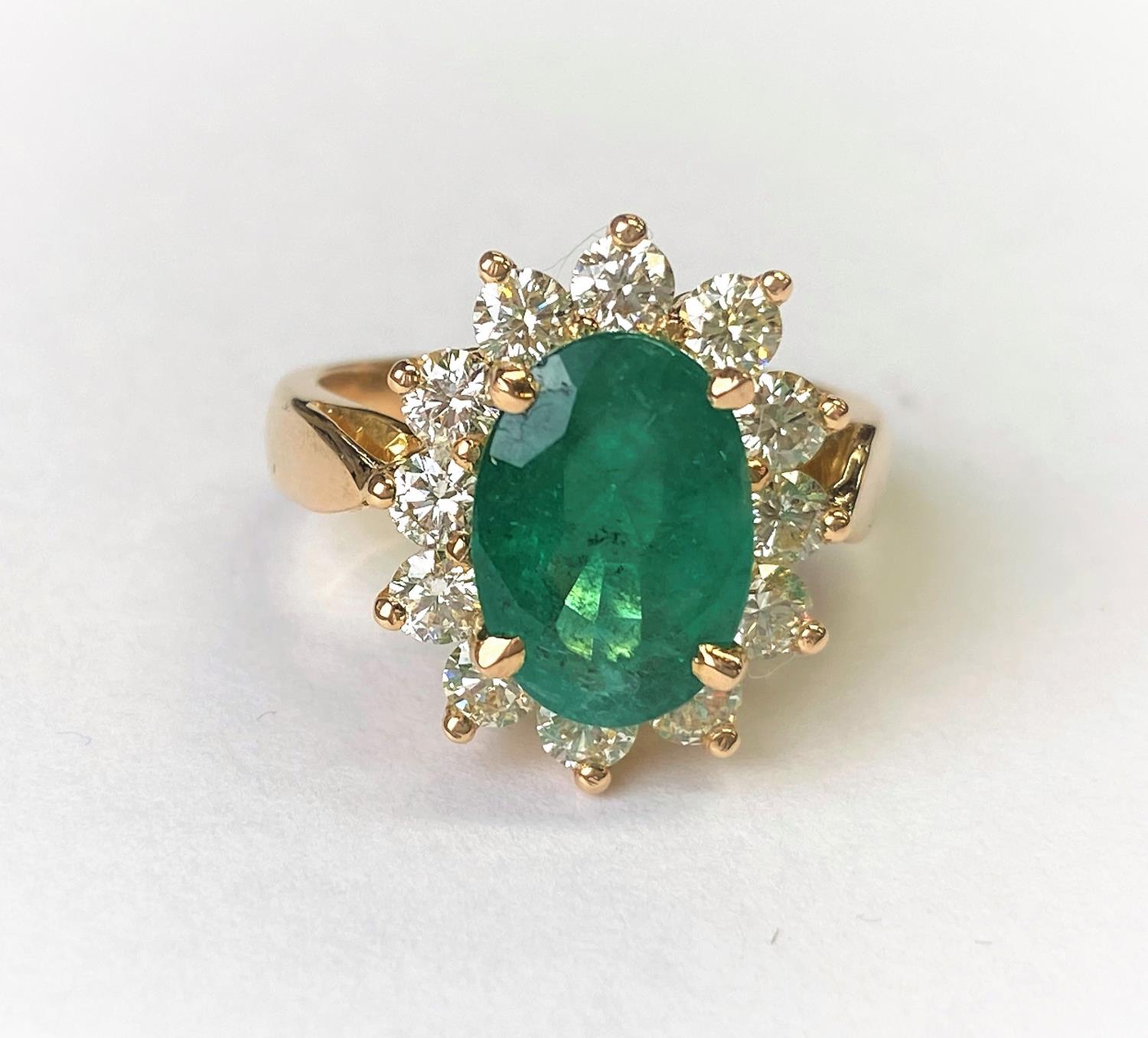 An 18ct gold dress ring set with a large faceted oval emerald, 11mm x 7mm and surrounded by 12