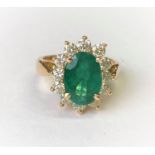 An 18ct gold dress ring set with a large faceted oval emerald, 11mm x 7mm and surrounded by 12