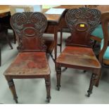 A pair of mahogany hall chairs with carved backs, solid seats and tapering carved legs