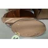 A circular floral etched peach framed wall mirror; an oval peach framed wall mirror
