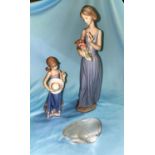 A Lladro figure, girl with hat; a Nao figure, woman with flowers; a glass otter, signed in script; a