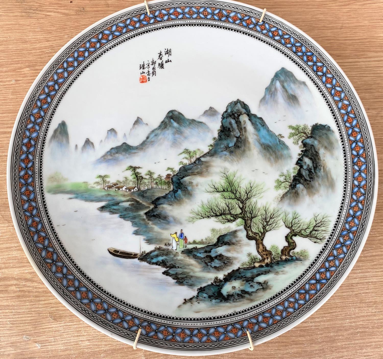 A 20th century Chinese hand painted charger decorated with mountain scenes, with text to top, seal