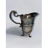 A hallmarked silver cream jug, helmet shaped on triple feet, Sheffield 1926