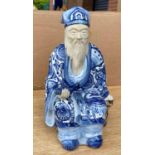 A Chinese figure of a seated man with beard in blue and white glazed robes, impressed mark to