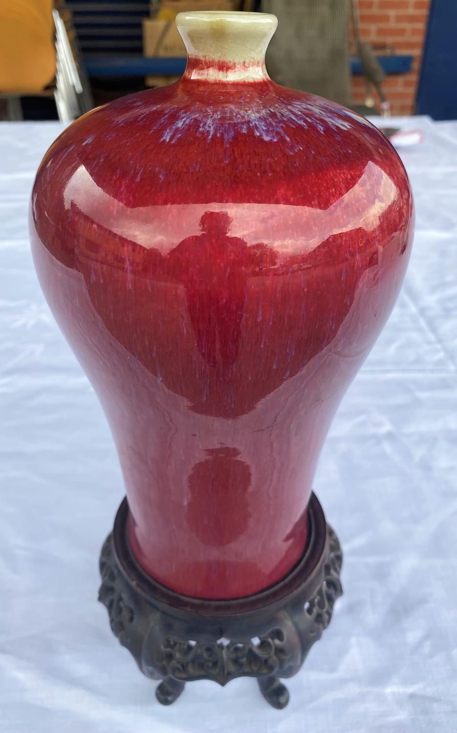 A Chinese sang de boeuf glaze inverted baluster vase on wooden stand, height of vase 21cm, height of
