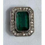 A rectangular cushion cut emerald coloured stone, surrounded by small diamonds.