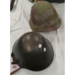 A steel combat helmet with leather and nylon lining, another helmet with a canvas camouflage cover.