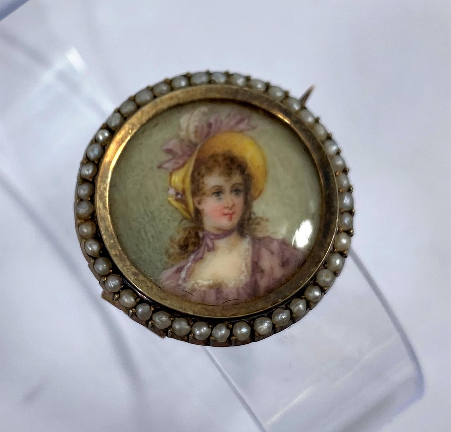 A brooch with half length miniature portrait of a young woman in a bonnet, bordered by seed