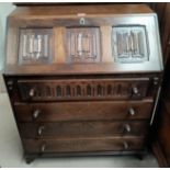 A reproduction oak bureau with linen fold carving, fall front and 4 drawers