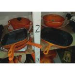 A selection of Le Creuset and similar style cast metal cooking ware in orange, with a wooden pan