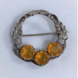 A circular hallmarked silver brooch decorated with thistles in relief and set with three amber