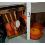 A selection of Le Creuset and similar style cast metal cooking ware in orange, with a wooden pan