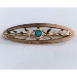 An oval yellow metal brooch set with a central turquoise stone flanked by leaves, stamped T G,