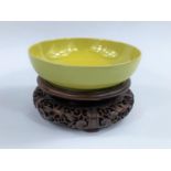 A Chinese yellow glaze shallow bowl with seal mark to base, on a hardwood carved stand, diameter