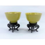 A pair of Chinese yellow glaze rice bowls, on hardwood stands, with seal mark to bases, diameter