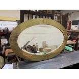 An Arts and Crafts brass applied oval wall mirror with bevelled plate. 32' wide