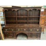 An antique joined oak dresser, the raised rack over three drawers and cupboards flanking and