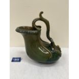 A 19th century green glazed pottery ewer of organic form with acanthus and figure moulded handle.