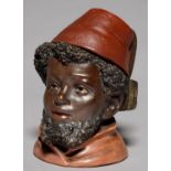 A CONTINENTAL COLD PAINTED TERRACOTTA TOBACCO JAR AND COVER IN THE FORM OF THE HEAD OF A BLACK