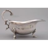 A GEORGE V SILVER SAUCE BOAT WITH LEAF CAPPED FLYING SCROLL HANDLE ON THREE HOOF FEET, INITIALLED W,