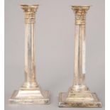 A PAIR OF SILVER COLUMNAR CANDLESTICKS, WITH CORINTHIAN CAPITAL ON BEADED SQUARE FOOT, NOZZLES, 26.