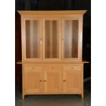A MODERN PALE OAK BOOKCASE-CUPBOARD WITH FLARED DENTIL MOULDED CORNICE ABOVE GLAZED DOORS AND
