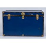 A BRASS BOUND BLUE REXINE COVERED PLY TRUNK WITH BLACK PLASTIC STUDDED BORDERS, LACQUERED GILT WHITE