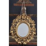 A FLORENTINE GILTWOOD MIRROR, 19TH C, WITH BEVELLED OVAL PLATE AND BEADED SURROUND, THE FRAME CARVED