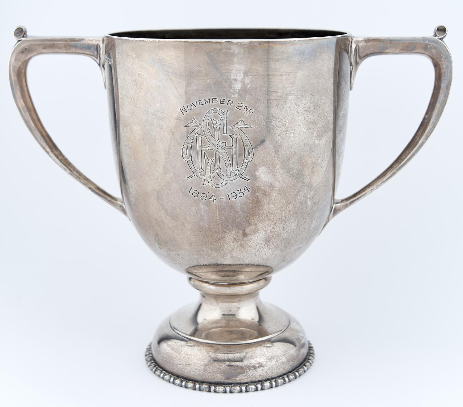 A GEORGE V SILVER CUP OF SHIELD SHAPE WITH ANGULAR HANDLES, ON DOMED FOOT WITH BEADED WRIM, ENGRAVED