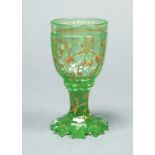 A BOHEMIAN GREEN GLASS GOBLET, C1860, THE FACETED BOWL AND WAISTED STEM WITH RAISED GILT SCROLLING