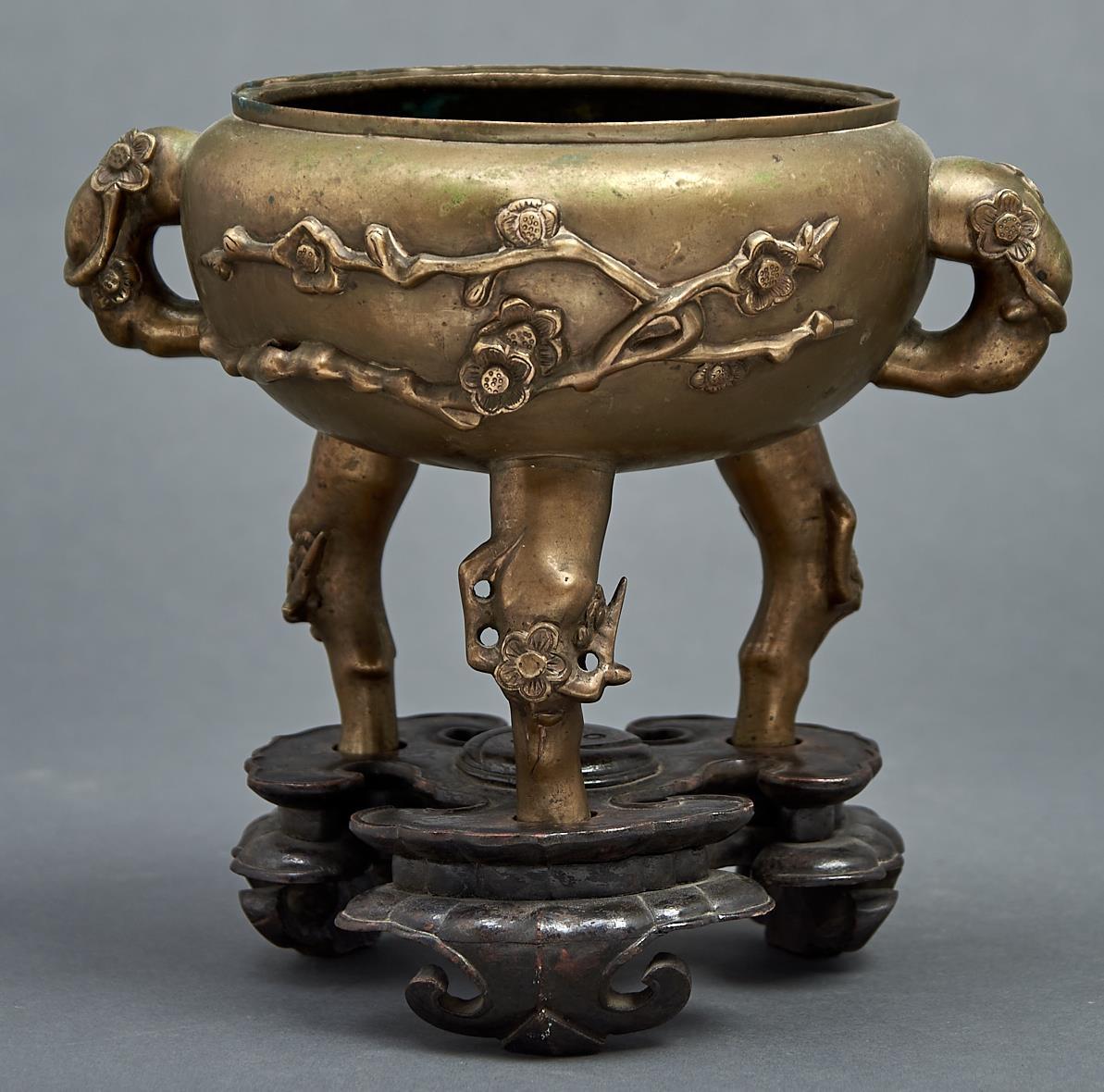 A Chinese bronze tripod censer, 19th c, cast with prunus, 17cm h, commendation mark, wood stand