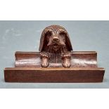 A Swiss carved and stained limewood dog's head novelty inkwell and pen rest, c1900, with black