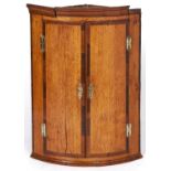 A George III inlaid oak bow fronted corner cupboard, 95cm h x 70cm w Shrinkage cracks to one door,