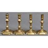 Two pairs of George II brass candlesticks, mid 18th c, with waisted or cylindrical sconce,