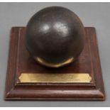 A 12cm diam cast iron cannonball,  17th c, mounted on a mahogany square plinth bearing brass plate