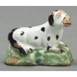 A Dutch polychrome Delft miniature model of a dog, c1770, painted in manganese and red, lying on a