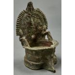 A Nepalese bronze oil lamp , the shaped back cast with seated cross legged female Bodhisattva within