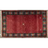 A modern woollen rug, the red ground worked with central stylised figure and animals to the