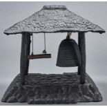 A South East Asian black painted cast metal gong, in the form of a temple bell beneath thatched