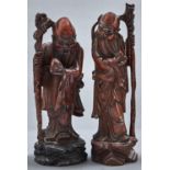 A pair of Chinese hardwood figures of bearded immortals, each standing holding a fruit and staff,