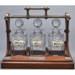 An Edwardian oxidised brass mounted oak tantalus, Grinsell's Patent, containing three cut glass