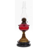 An Edwardian brass oil lamp, embossed with leaves, cranberry glass fount, on black glazed