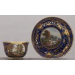 A Derby blue ground teacup and saucer, c1820, painted with figures by a river or in a clearing,