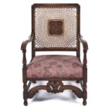 An upholstered beech nursing chair, c1930's, the caned back with central cantered square foliate