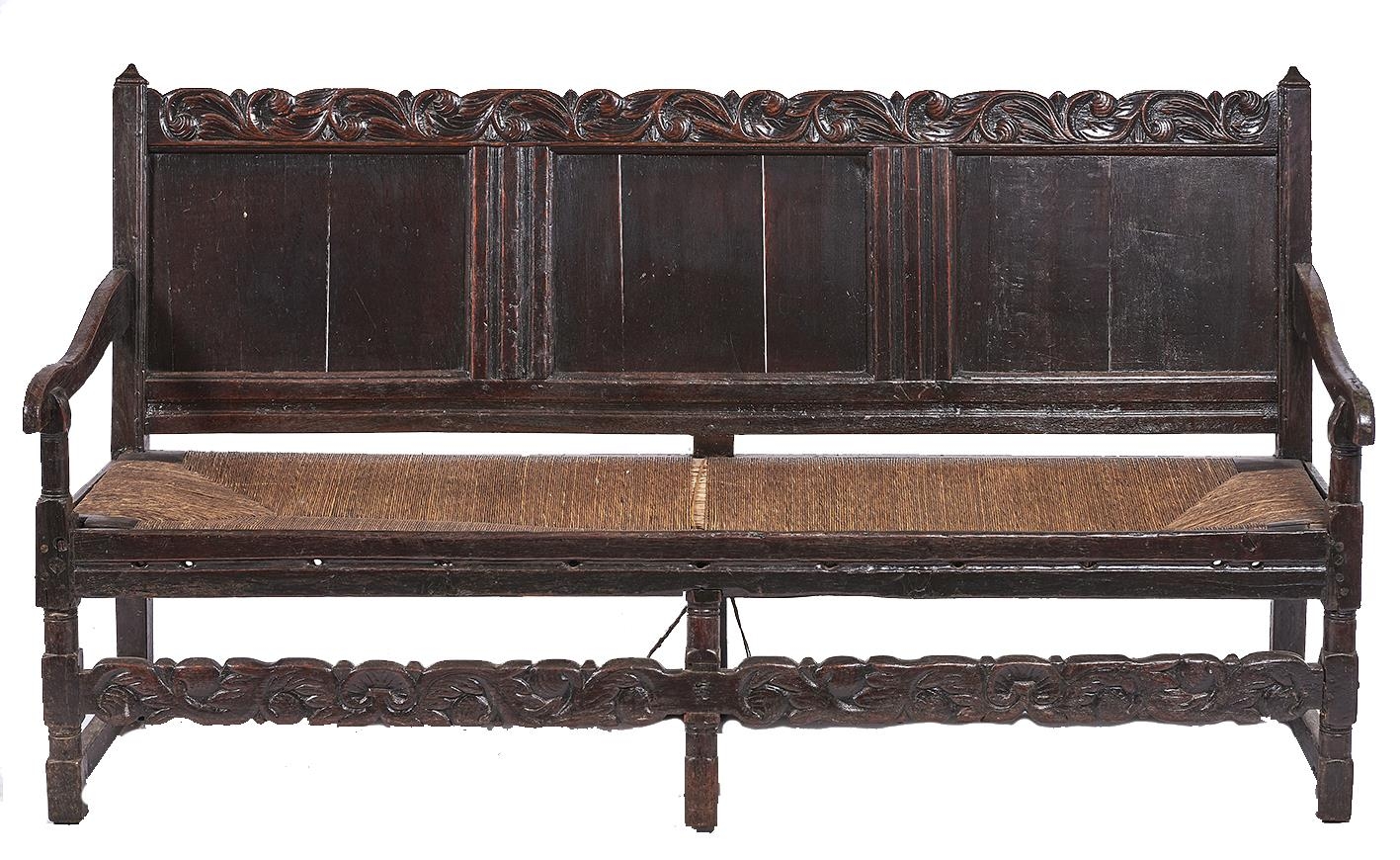 A Charles II panelled oak settle, late 17th c, with boldly carved leafy scrolling crest rail and