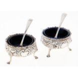 A pair of Victorian silver salt cellars, chased with flowers and c-scrolls, on three hoof feet, blue