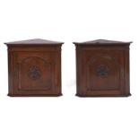 A pair of oak hanging corner cupboards, 20th c, the interior with serpentine shelf enclosed by a