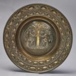 An embossed brass alms dish, the raised centre with the seated figures of Adam and Eve at the Tree