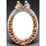 A German porcelain dressing mirror, late 19th c,  the oval frame encrusted with strawberries and