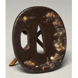 A Japanese iron tsuba, Edo period, carved and decorated in gold with two seated figures, plants